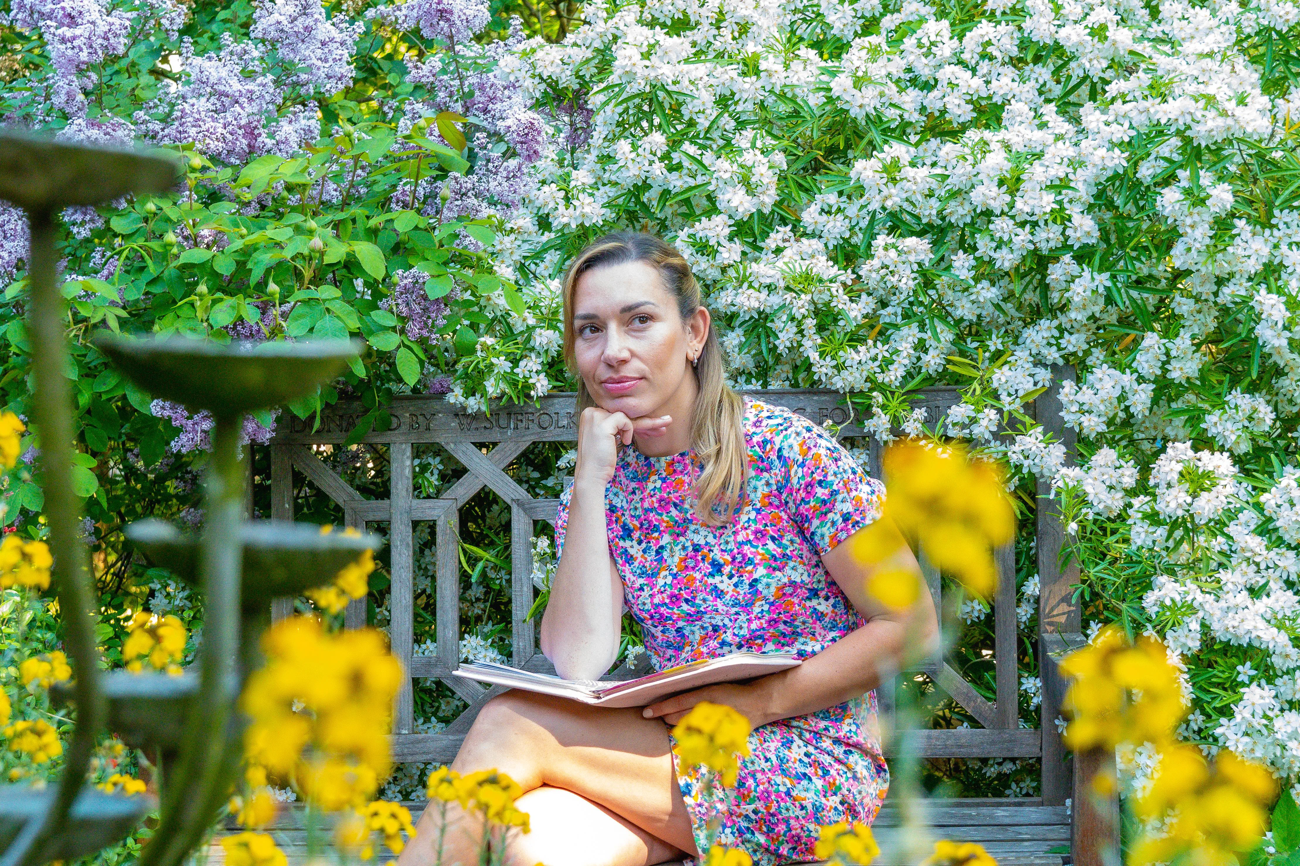 A female coach in a colourful dress poses in a brigth garden